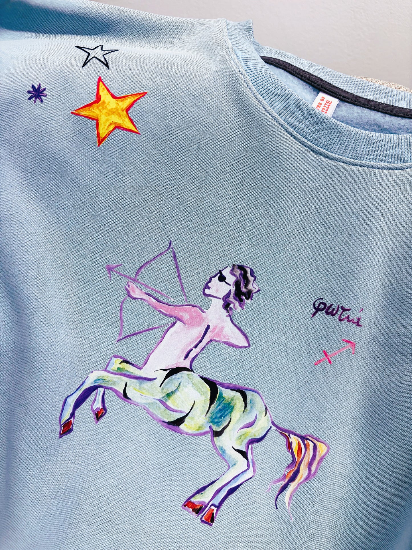 100% βαμβακερό φούτερ ελληνικής ραφής με πολύχρωμα τυπώματα μπροστά, πίσω και στα δύο μανίκια με θέμα το ζώδιο του Τοξότη σε γαλάζιο χρώμα.