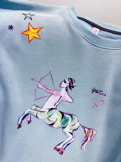 100% βαμβακερό φούτερ ελληνικής ραφής με πολύχρωμα τυπώματα μπροστά, πίσω και στα δύο μανίκια με θέμα το ζώδιο του Τοξότη σε γαλάζιο χρώμα.